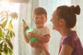 Plant care concept. Cheerful little male kid holds spray bottle, wants to water flower, stands neear his affectionate mother near Royalty Free Stock Photo