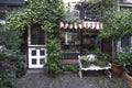 The plant-covered entrance to a small hidden and cozy shop. White door and window frames. An awning protects the window. in front Royalty Free Stock Photo