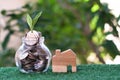 Plant growing from coins in glass jar. Wooden house model on artificial grass. Home mortgage and property investment concept Royalty Free Stock Photo