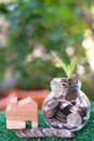 Plant growing from coins in glass jar. Wooden house model on artificial grass. Home mortgage and property investment concept Royalty Free Stock Photo