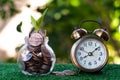 Plant growing from pile of coins with vintage clock beside. Time is money. Savings and investment concept. Copy space Royalty Free Stock Photo