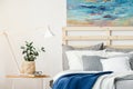 Plant and lamp on table next to bed with blue blanket in bedroom Royalty Free Stock Photo