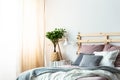 Plant and lamp on table next to wooden bed with pink and grey cu