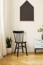 Black chair against white wall with poster in living room interior with cabinet. Real photo Royalty Free Stock Photo