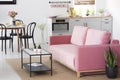 Plant next to pink sofa in apartment interior with chairs at din