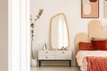 Plant next to white dressing table with mirror in red bedroom in