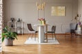 Plant and painting in grey open space interior with chairs at dining table under gold lamp. Real photo