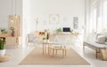 Plant on pouf neat wooden tables on brown carpet in spacious white flat interior with sofa. Real photo