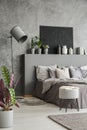 Plant, stool and lamp in modern grey bedroom interior with poster above bed. Real photo Royalty Free Stock Photo