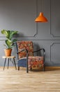 Plant on table next to patterned armchair under orange lamp in g