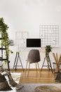 Plant, white lamp and desktop computer on desk in freelancer`s interior with grey chair. Real photo Royalty Free Stock Photo