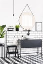 Plants and mirror in black and white bathroom interior with checkered floor and stool. Real photo