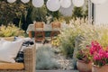 Plants next to rattan sofa with pillows on the terrace with wooden chairs at table