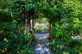 Plants overgrown on trellis in garden with path leading through door to bench and pond Royalty Free Stock Photo