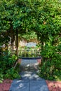 Plants overgrown on trellis in garden with path leading through door to pond with bench Royalty Free Stock Photo