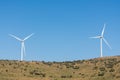 A pair of windmills on a clear blue sky in the Sierra del Merengue next to a meadow with cows in Plasencia.