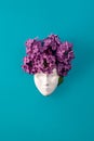 Plaster face, figurine decorated with lilac flowers. Lilac as a hairstyle on the head figurine against blue background