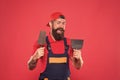 Plasterer hipster builder in cap red background. Interior designer. Bearded man worker with plastering tools