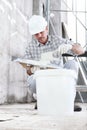 Plasterer man at work, take the mortar from the bucket to plastering the wall of interior construction site wear helmet and Royalty Free Stock Photo