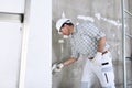 Plasterer man at work with trowel plastering the wall of interior construction site wear helmet and protective gloves, ladder and Royalty Free Stock Photo