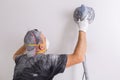 Plasterer wearing dust mask polishes a wall with sanding machine Royalty Free Stock Photo