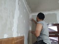 Plasterwork and wall painting preparation. Asian male applying plaster or filling drywall patch