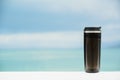 Plastic black thermos mug without handle on blurred sea and sky background Royalty Free Stock Photo