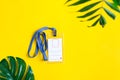 Plastic blank mock-up name tag on a yellow background with green tropical leaves. Top view. Royalty Free Stock Photo