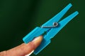 plastic blue clothes peg pinching hand index finger under green background