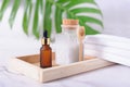 Plastic bottle filled with white bath sea salt and wooden spoon, amber color dropper and white towels on wooden tray Royalty Free Stock Photo