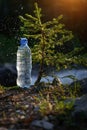 Plastic bottle with fresh icy drinking water on blur background of small tree and mountain river. Jet falls on the bottle, Royalty Free Stock Photo
