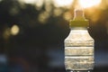 Plastic bottle top full with water with yellow cap in a park or garden with green trees in blurred background Recyclable beverage Royalty Free Stock Photo