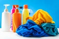 Plastic bottles of cleaning products set with pile clothes on white table blue background Royalty Free Stock Photo