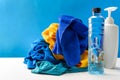 Plastic bottles of cleaning products set with pile clothes on white table blue background Royalty Free Stock Photo