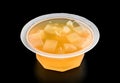 Plastic bowl with orange jelly and pieces of fruit close-up isolated on black background