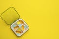 Plastic box with different pills on yellow, top view. Space for text Royalty Free Stock Photo