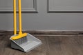 Plastic broom with dustpan near grey wall indoors. space for text