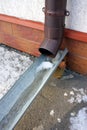 Plastic brown downspout with frozen rainwater in winter. Roof drain pipe. Waterspout. Water roofing rain pipeline.