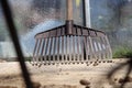 A plastic brown rake leaning against greenhouse. Also with small stones and view is between some iron sticks Royalty Free Stock Photo