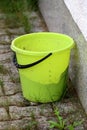 Plastic bucket with black handle left behind house on stone tiles with grass growing between