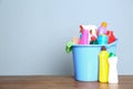 Plastic bucket with different cleaning products on table against color background Royalty Free Stock Photo