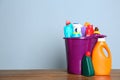 Plastic bucket with different cleaning products on table against color background Royalty Free Stock Photo