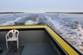 A plastic chair sitting in the back of a fishing boat on a calm bay in the late afternoon with a wake behind Royalty Free Stock Photo