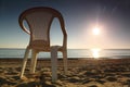 Plastic chair stands sideways on beach near sea