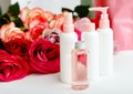 Plastic cosmetic bottles, serum, soap, oil on white table floral background. Flower red pink roses natural organic beauty product
