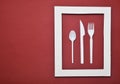 Plastic cutlery for picnics in a white frame on a red background. A disposable spoon, fork, knife. Top view, minimalistic trend Royalty Free Stock Photo