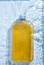 A plastic drink cold clear bottle is placed in the water pool. Transparent blue colored clear water surface texture with ripples, Royalty Free Stock Photo