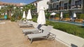 Plastic and fabric umbrellas and lounge chairs are set up on a tiled area near the lawn and pool, surrounded by buildings with bal Royalty Free Stock Photo