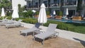 Plastic and fabric umbrellas and lounge chairs are set up on a tiled area near the lawn and pool, surrounded by palm trees and bui Royalty Free Stock Photo