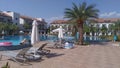 Plastic and fabric umbrellas and lounge chairs are spread out on the tiled pool deck surrounded by buildings with balconies and pa Royalty Free Stock Photo